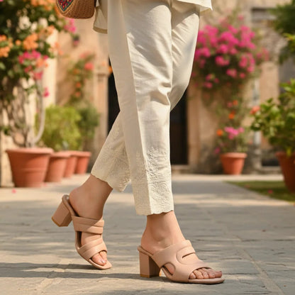 Person wearing beige sandals and white pants walking on a stone path with flowers and plants in the background.
